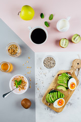 Healthy Breakfast concept. Sandwich with avocado and boiled eggs, yogurt with granola, cup of coffee over tricolor stylish background, top view, flat lay. Health, weight loss, diet food concept