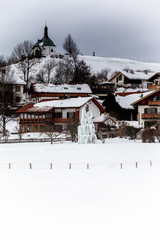 Krieger-Gedächtniskapelle Bad Bayersoien im Winter, im Vordergrund ein zu Eis gefrorener Baum in den Ammergauer Alpen