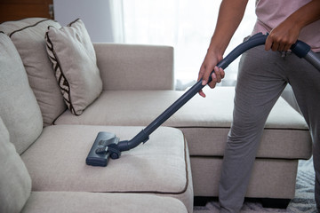 close up of man's hand cleaning couch using vacuum cleaner at home