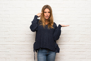 Blonde woman over brick wall making the gesture of madness putting finger on the head