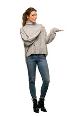 A full-length shot of a Blonde woman with turtleneck holding copyspace imaginary on the palm to...
