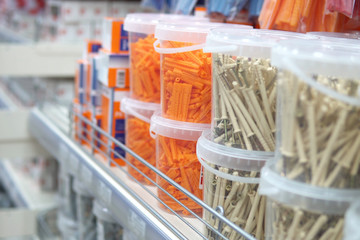 Transparent containers with orange plastic fixing wall plugs and grey dowel-nails on shelf of...