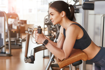 Perfect exercise program. Side view of sporty and beautiful young woman in sportswear and with smart watch on her hand working out at gym.