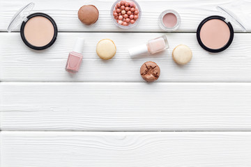 decorative cosmetics for make-up with macaroon cookies on white wooden tabletop background mock up