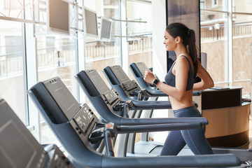 Body improvement. Side view of young and beautiful woman in sportswear running on a treadmill at...