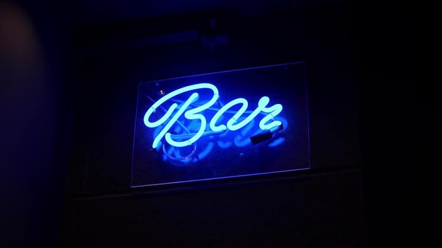 A close up shot of a bright blue neon Bar sign, the blue glows on a black brick background, the light is ultra vibrant which is noticeable for any passerby looking explore the night& visit the bar
