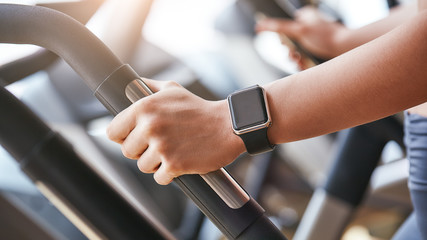 Smart technologies. Close-up photo of smart watch on woman hand holding the handle of cardio...