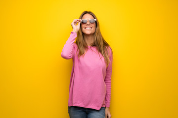 Woman with pink sweater over yellow wall with glasses and surprised