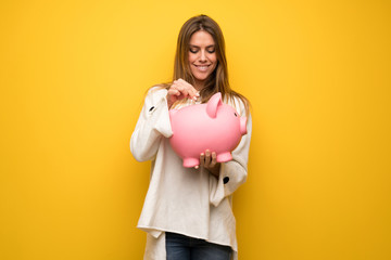 Fototapeta na wymiar Blonde woman over yellow wall taking a piggy bank and happy because it is full