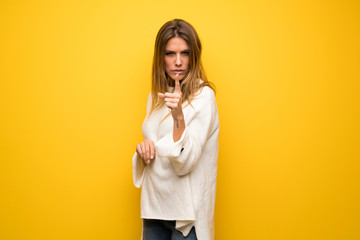 Blonde woman over yellow wall frustrated and pointing to the front
