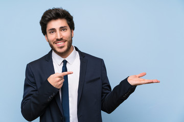 Businessman over isolated blue wall holding copyspace imaginary on the palm to insert an ad
