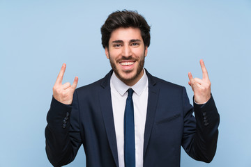 Businessman over isolated blue wall making rock gesture