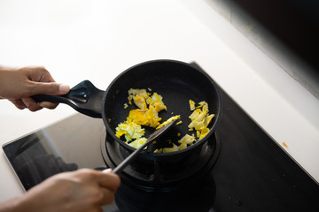 Close up of hands holding spatula to stir fry scrambled eggs carefully on hot pan
