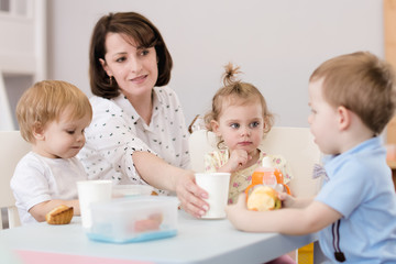 Obraz na płótnie Canvas kids have lunch with teacher in nursery