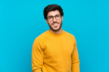 Handsome over isolated blue wall with glasses and happy