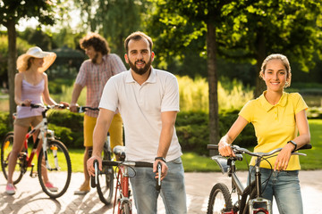 Obraz premium Young students with bicycles outdoors. Smiling tourists with bicycles at summer park. People, tourism and active lifestyle.