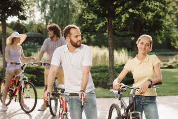 Man and woman with bicycles in park. Young stylish couple riding bikes outdoors. Summer date on bicycles.