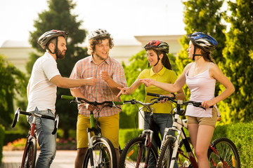 Fototapeta na wymiar Young people having fun together outdoors. Group of happy bikers playing rock-scissors-paper on summer nature background. Team of friends.