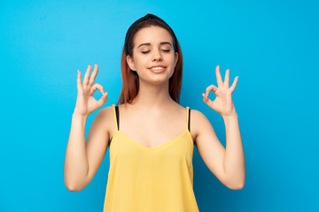 Young redhead woman over blue background in zen pose