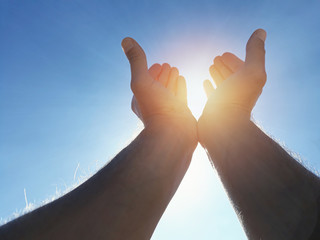 Male hands holding sun with blue sky.