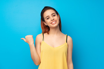 Young redhead woman over blue background pointing to the side to present a product