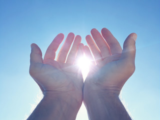 Male hands holding sun with blue sky.