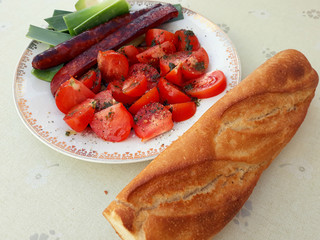 Baguette with tomatoes, sausage and vegetables on the table.