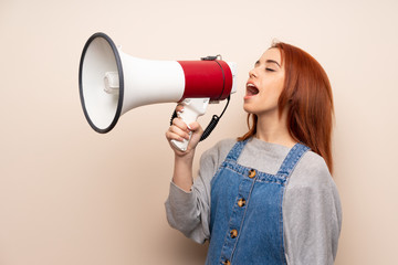 Young redhead woman over isolated background shouting through a megaphone