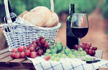 red wine ripe grapes and picnic basket on table in vineyard