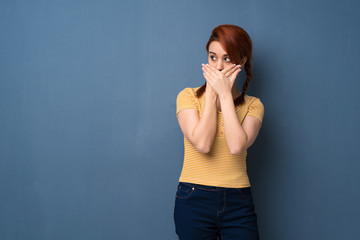 Young redhead woman over blue background covering mouth with hands