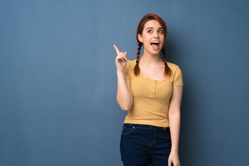 Fototapeta premium Young redhead woman over blue background intending to realizes the solution while lifting a finger up