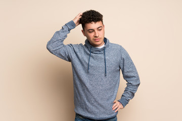 Young man over isolated wall having doubts while scratching head