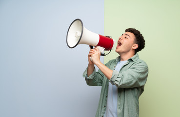 Young man over blue and green background shouting through a megaphone