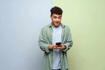 Young man over blue and green background sending a message with the mobile