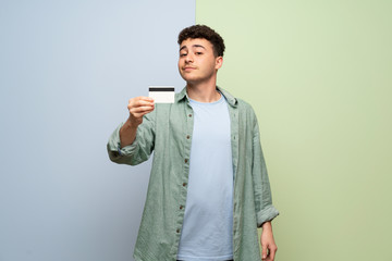 Young man over blue and green background holding a credit card