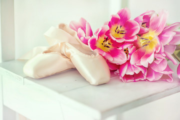 Pointe shoes with a delicate bouquet of tulips on a white wooden stool. General view.