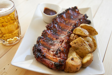 Grilled pork ribs with barbecue sauce, baked potatoes and beer mug.
