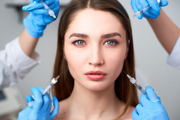 Hands of beauticians holding syringes around flawless woman face ready for injection in cosmetology...