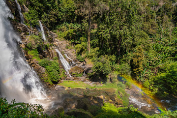 Fototapeta na wymiar Massive water stream falling in tropical forest with parts of rainbow 