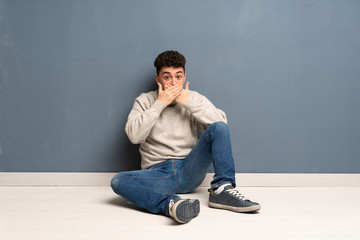 Young man sitting on the floor covering mouth with hands