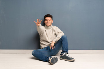 Young man sitting on the floor happy and counting four with fingers