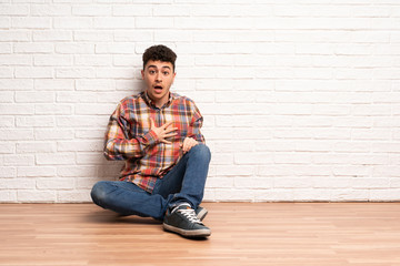 Young man sitting on the floor surprised and shocked while looking right