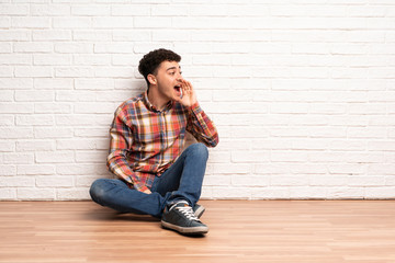 Young man sitting on the floor shouting with mouth wide open to the lateral