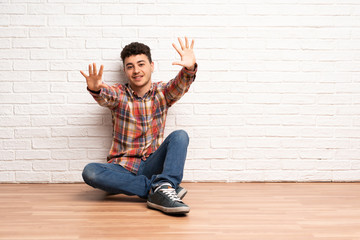 Young man sitting on the floor counting ten with fingers