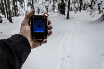 Man using a GPS device in a snowy forest. Hiker checking GPS information. Footprints