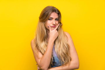 Obraz premium Young blonde woman with overalls over isolated yellow background standing and thinking an idea