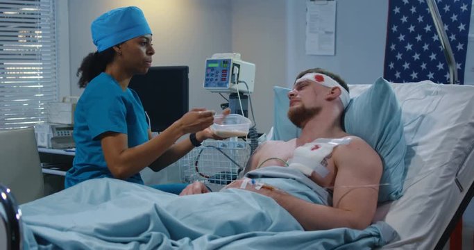 Nurse feeding injured soldier in hospital bed