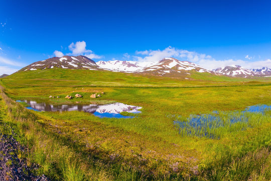 Summer Iceland. Blue lake water reflects snow hills