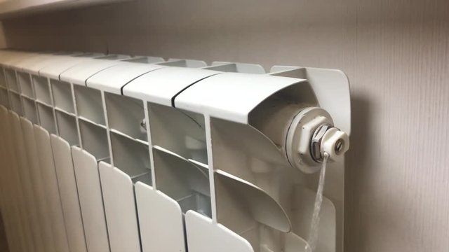 Airing of a heating radiator during repair. Water flows from a bimetal battery to generate heat. A small stream of water under pressure flows out of the hole. Repair work before the heating season.