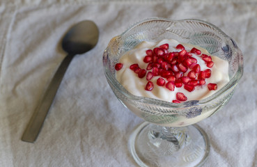 Natural yogurt topped with pomegranate seeds in decorative glass bowl - Healthy natural yoghurt background
